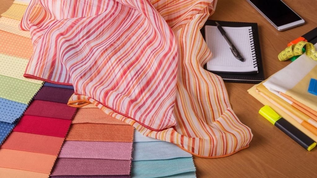 Fabric swatches and striped fabric on a desk with notepad and pen